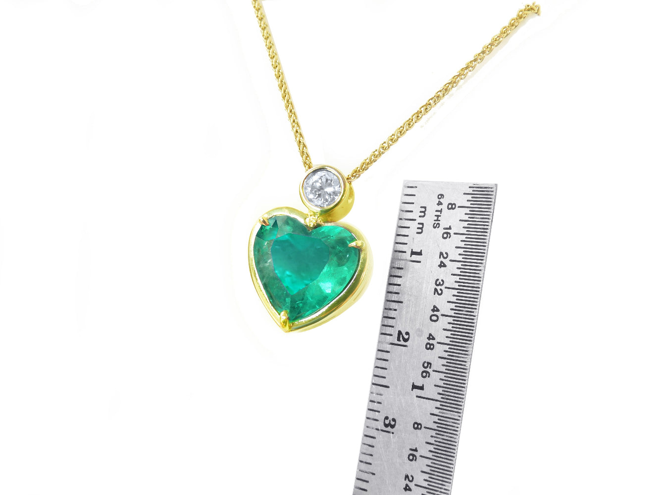 Gold necklace with a heart-shaped emerald pendant next to a ruler for scale on a white background