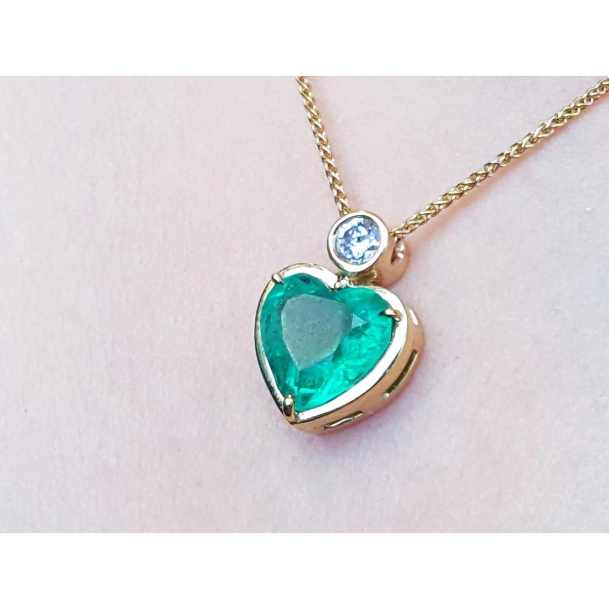 Heart-shaped emerald pendant on a gold chain against a light pink skin background
