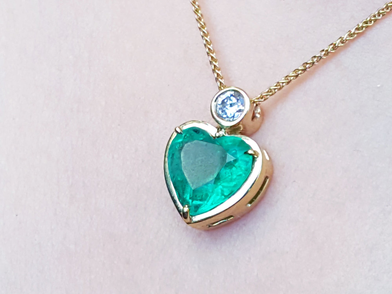 Heart-shaped emerald pendant on a gold chain against a light pink skin background