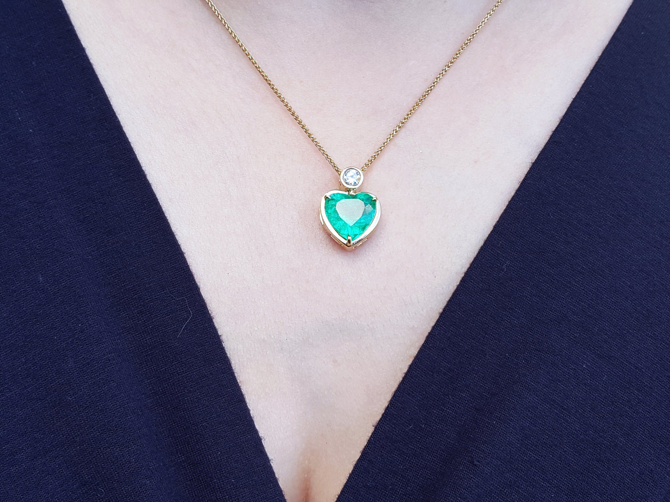 Necklace with a heart-shaped natural emerald gemstone pendant on a person wearing a dark blue top.