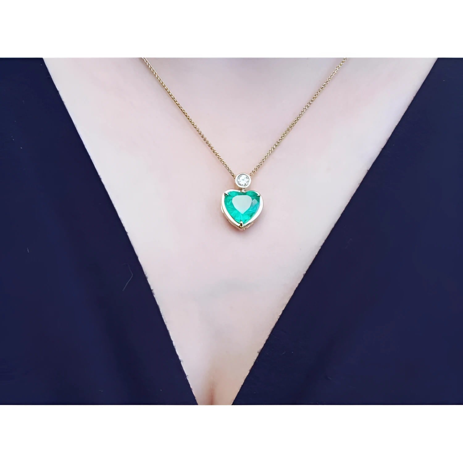 Heart-shaped emerald pendant necklace in 18K yellow gold with a diamond accent on a woman's neck.