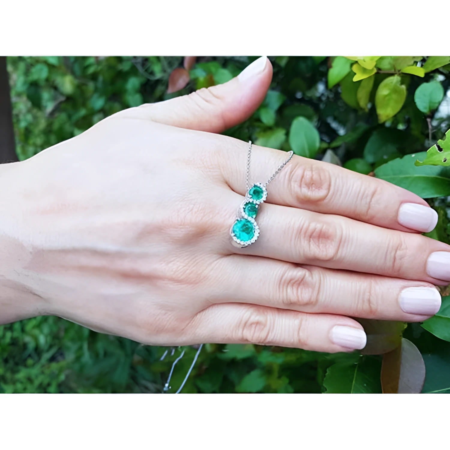 14K white gold emerald journey pendant with three round-cut Colombian emeralds and diamond halo.
