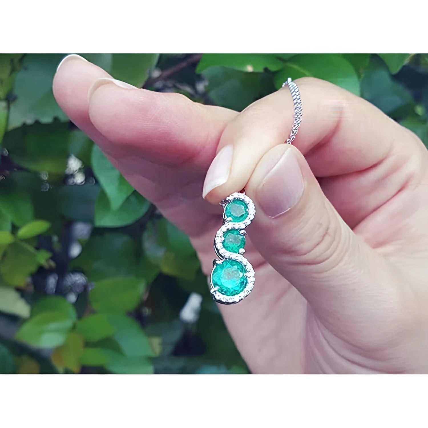 14K white gold emerald journey pendant with three round Colombian emeralds and diamond accents.