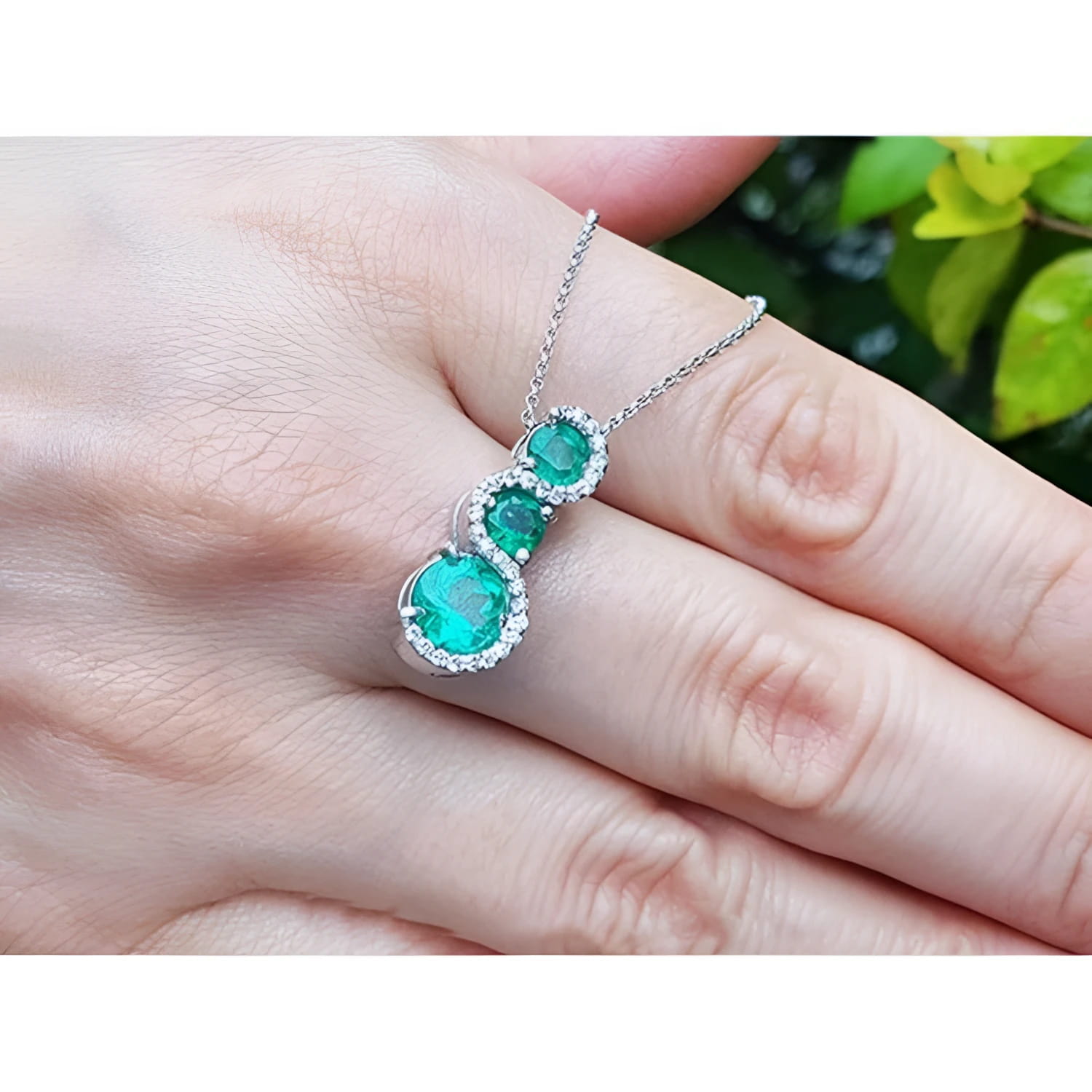 14K white gold emerald journey pendant necklace with three round green emeralds and diamond accents.