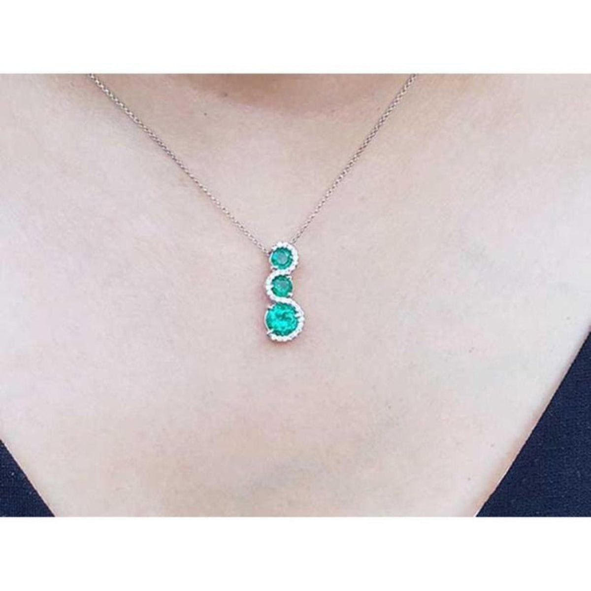 14K white gold journey pendant necklace with three round emeralds and diamond accents.