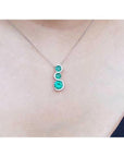 14K white gold journey pendant necklace with three round emeralds and diamond accents.