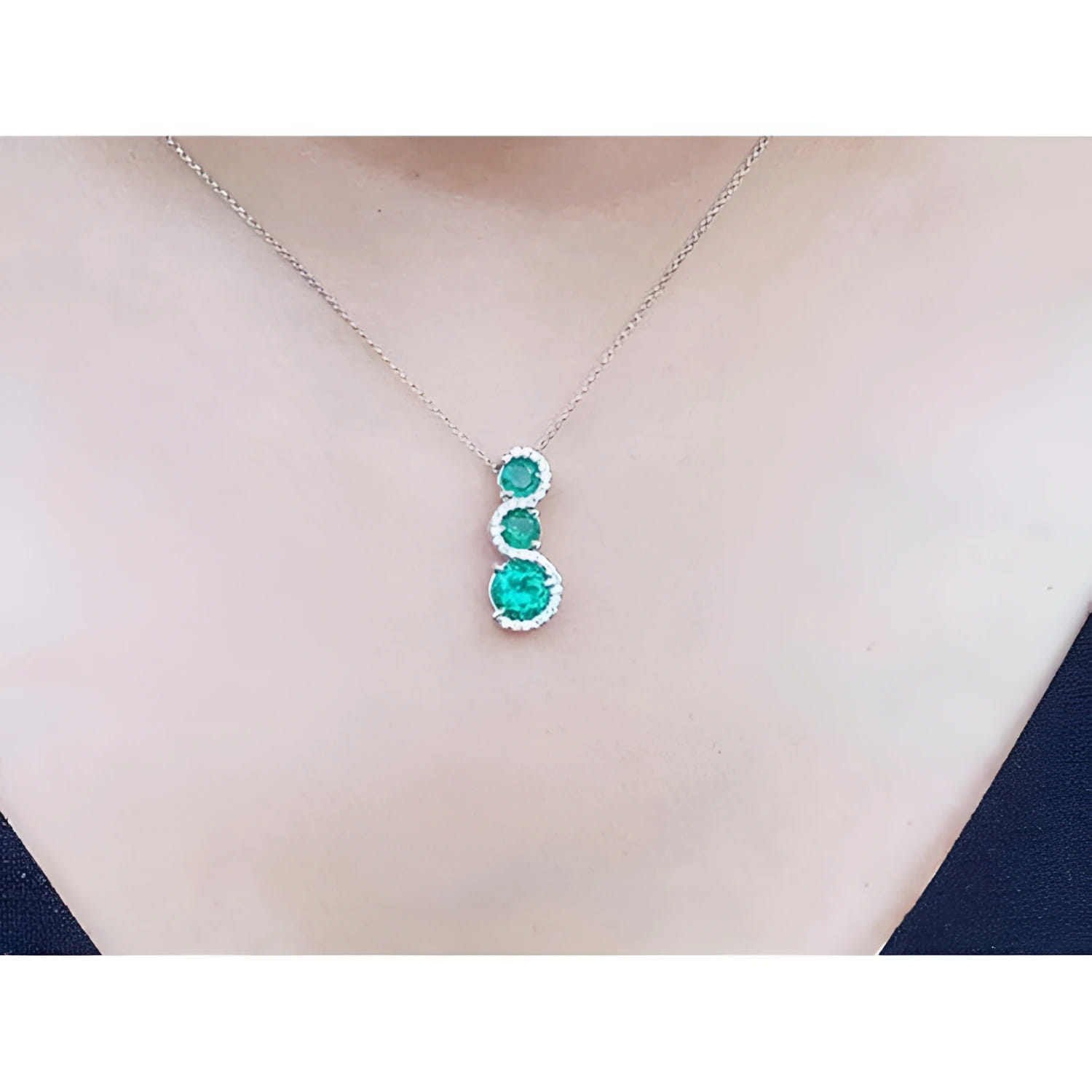14K white gold journey pendant necklace with three round emeralds and diamond accents.