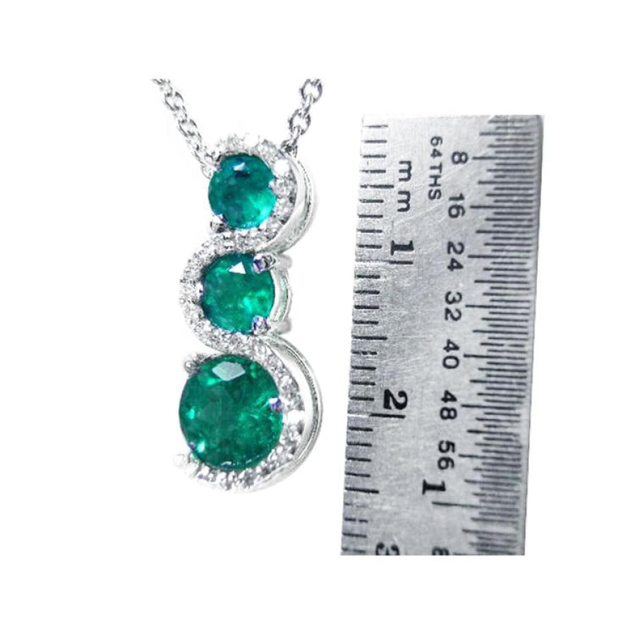 14K white gold emerald journey pendant with three round Colombian emeralds and diamonds on a twisted path.