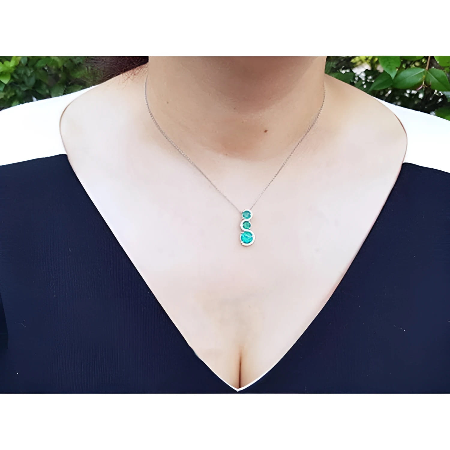 14K white gold emerald journey pendant necklace with three round deep green emeralds and diamonds.
