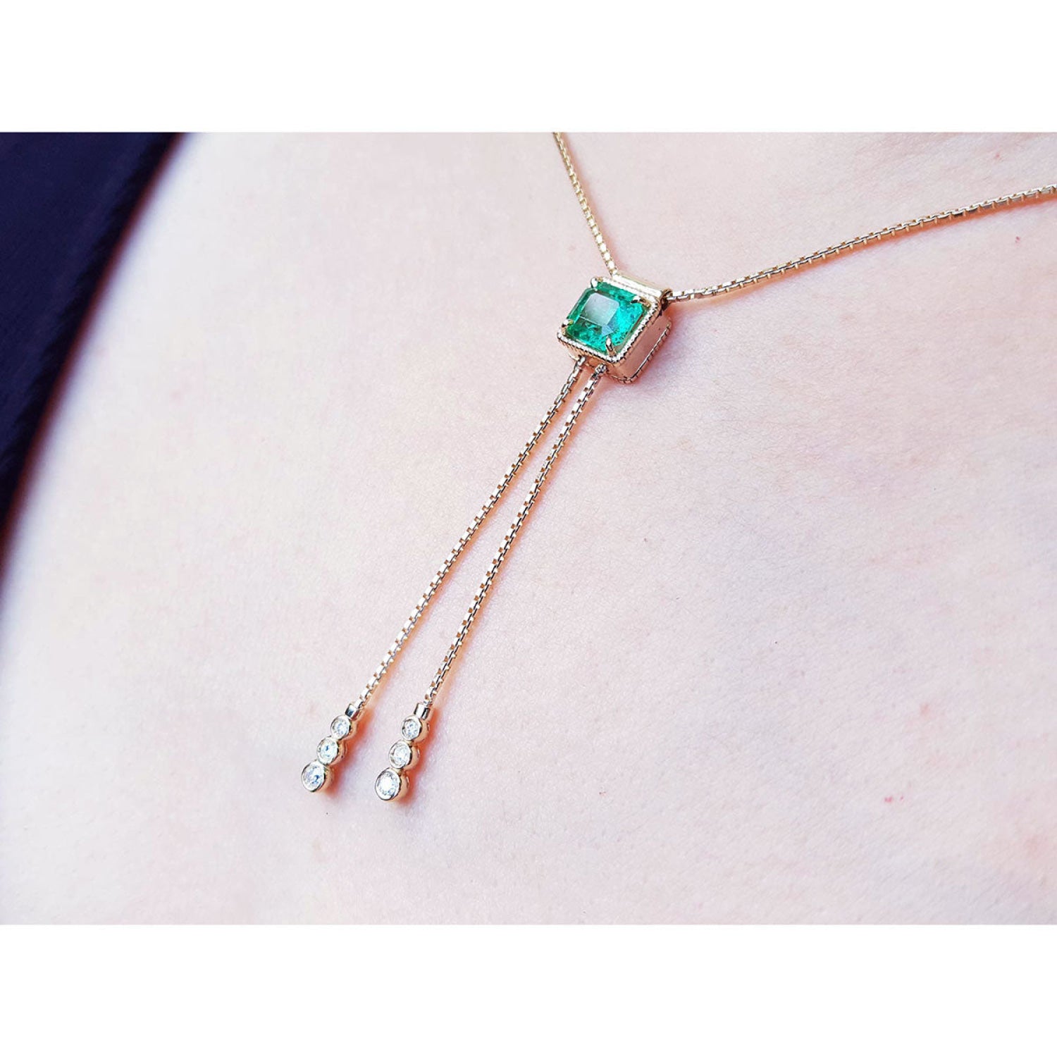 14K gold lariat necklace with a square emerald pendant and two dangling diamond accents on a box chain.