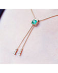 14K gold lariat necklace with a square emerald pendant and two dangling diamond accents on a box chain.