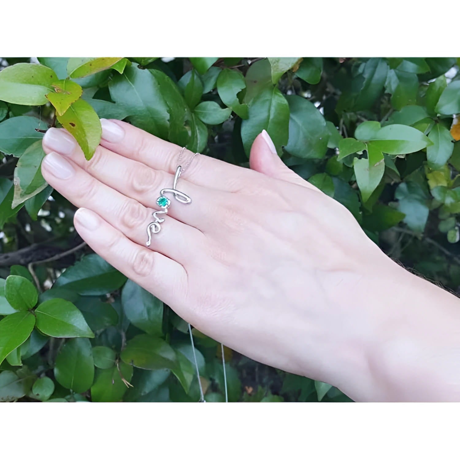14K white gold "love" script pendant necklace with a round Colombian emerald, worn on a hand.