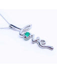 A 14k white gold necklace with a script love pendant featuring an emerald stone from Colombia.