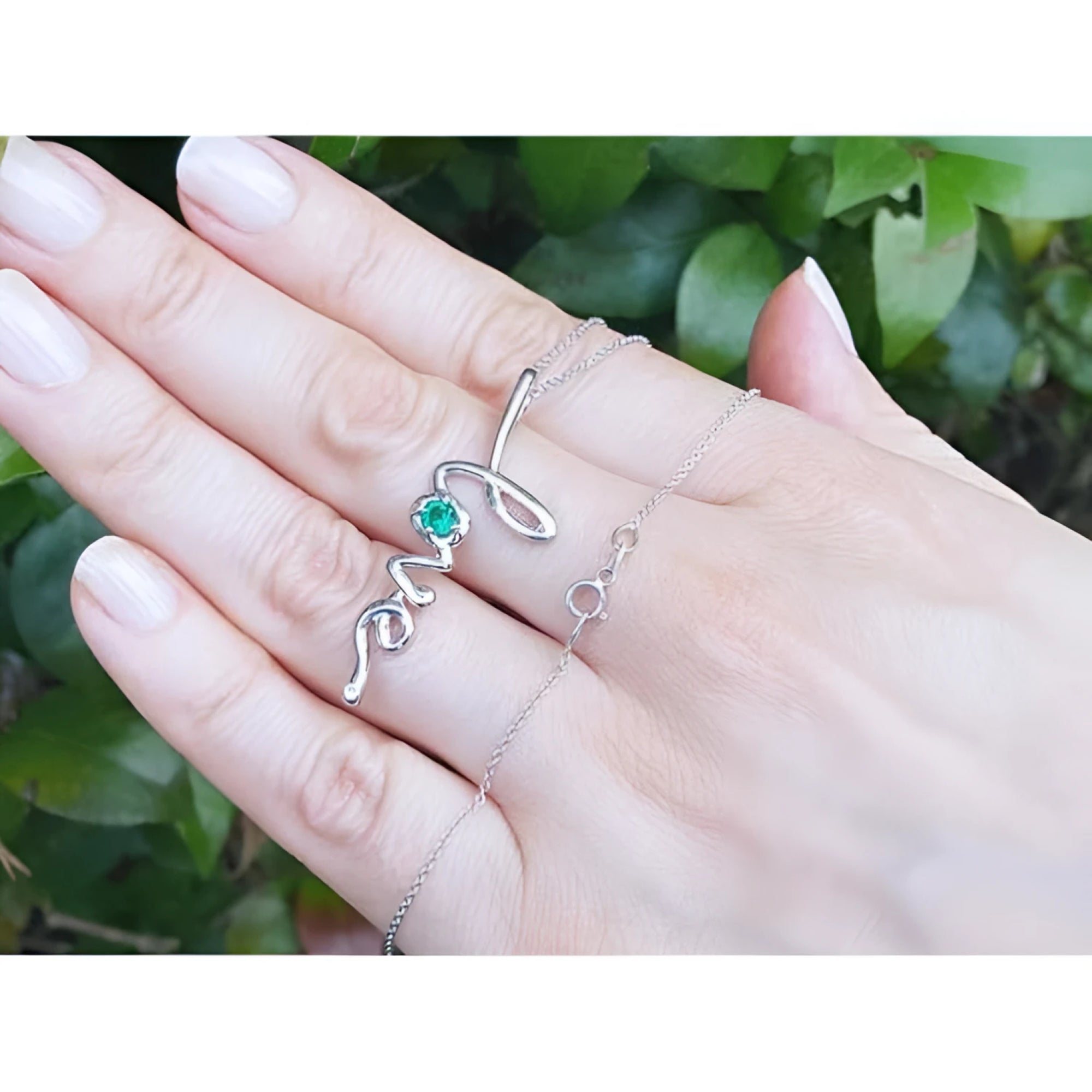 14K white gold "love" script pendant necklace with a round Colombian emerald, held on a hand.
