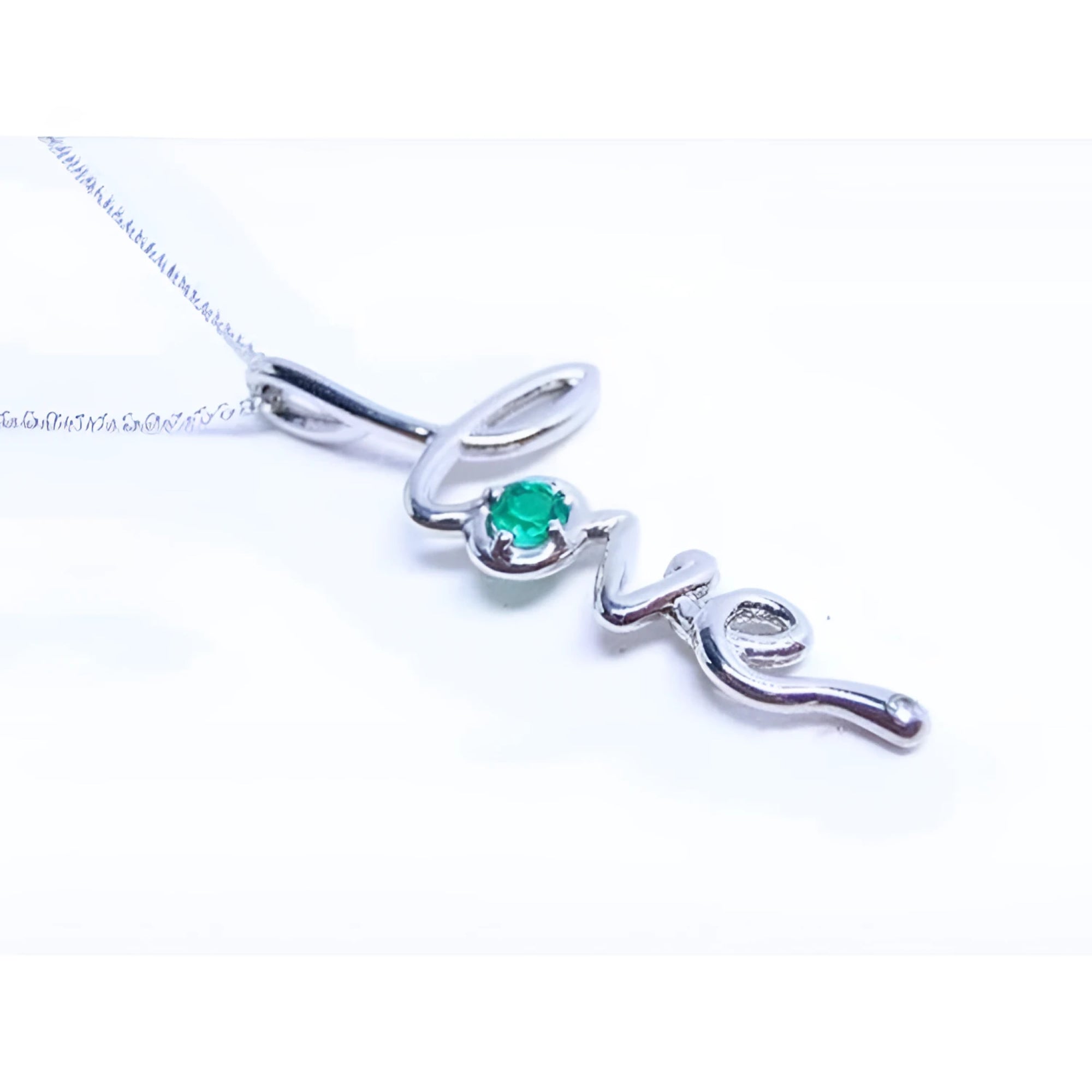 A white gold necklace with a script love pendant featuring an emerald stone on a white background.
