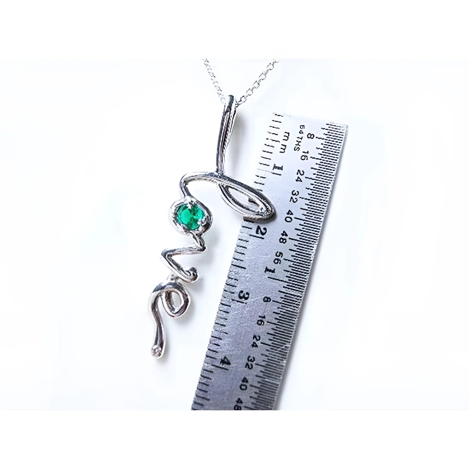 14K white gold "love" script pendant necklace with a round Colombian emerald, next to a ruler.