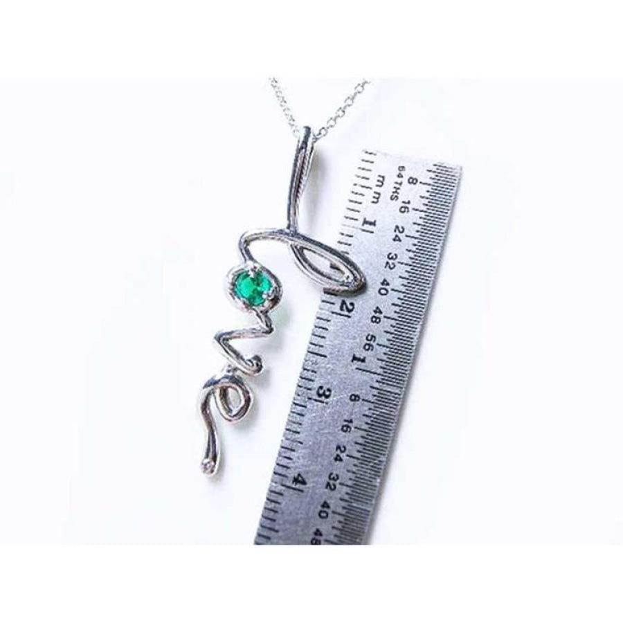 14K white gold "love" script pendant necklace with a round Colombian emerald, next to a ruler.