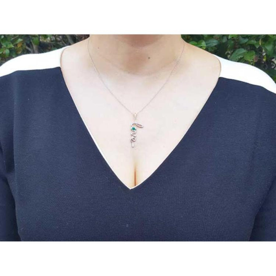 14K white gold "Love" script pendant with a round Colombian emerald, worn on a woman's neck.