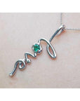 14K white gold "love" script pendant with a round Colombian emerald, on a delicate chain.