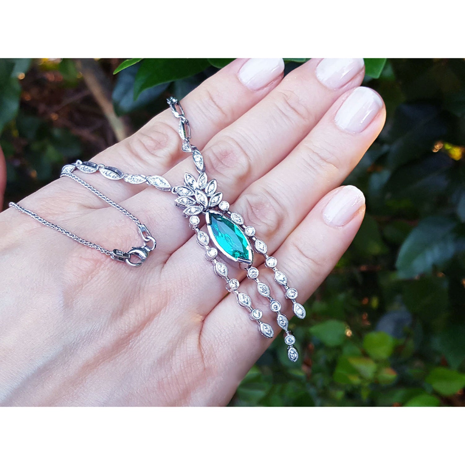 Marquise Colombian emerald and diamond necklace in 14K white gold, held in a hand.