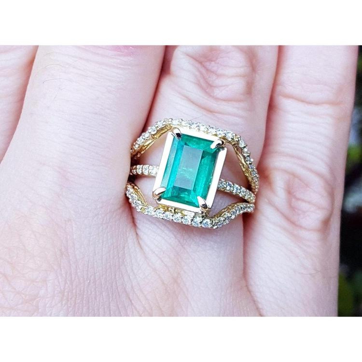 Emerald cut emerald engagement ring in 18K yellow gold with three rows of diamonds.