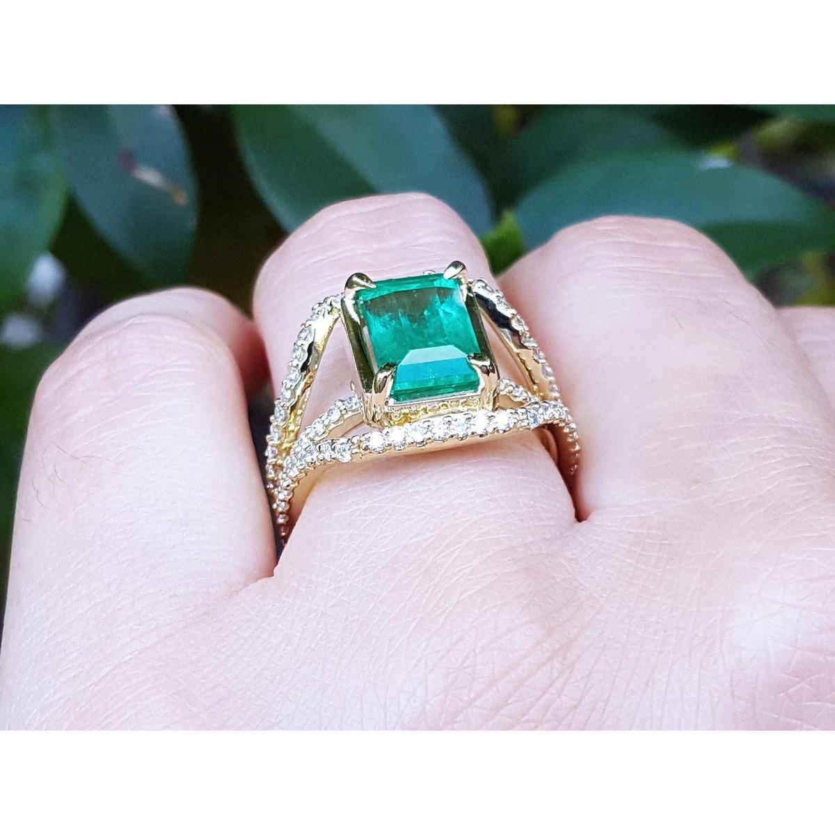 A yellow gold genuine emerald ring on a hand against a blurred natural background.