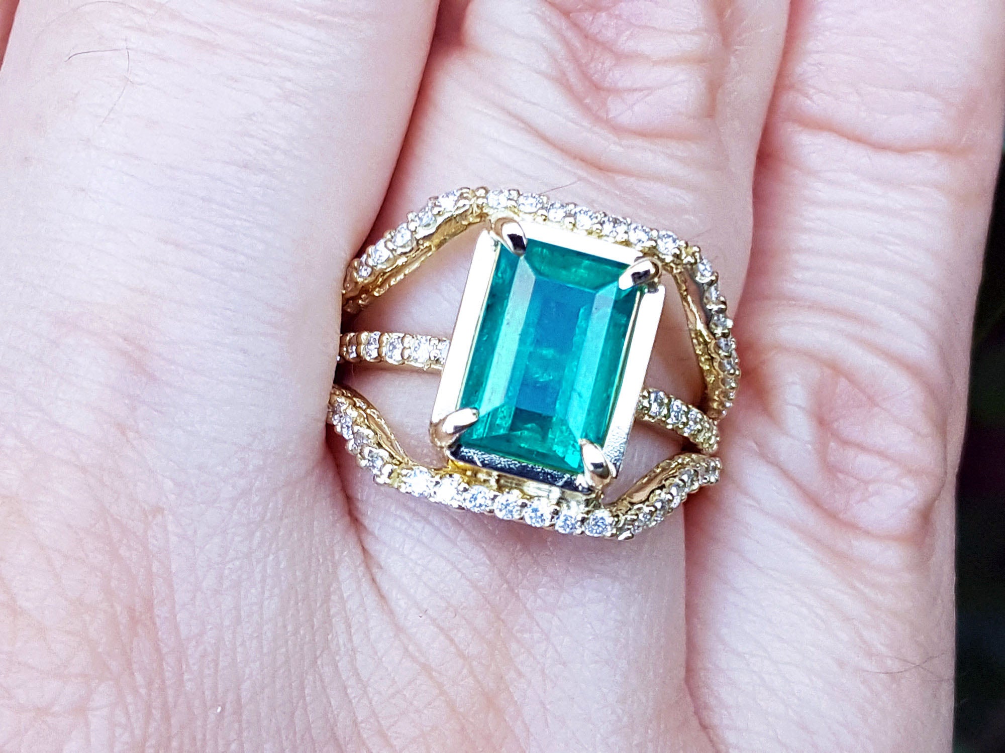 A close-up of an emerald ring on a finger top side view.