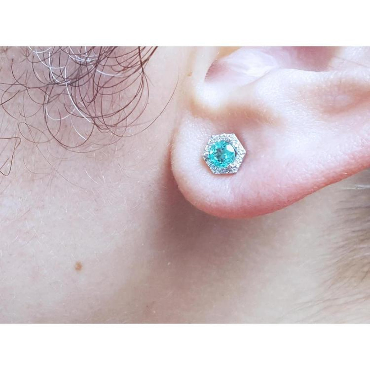 Emerald May birthstone stud earring in 14K white gold with a hexagonal halo on an earlobe.