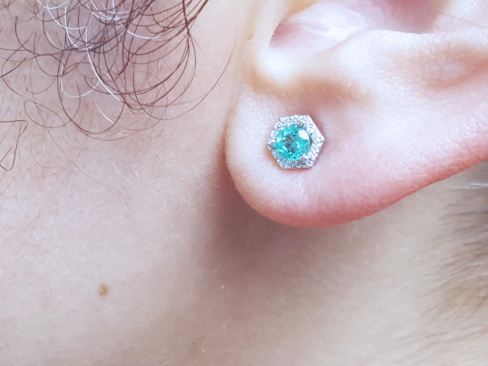 A close-up of a ear wearing a round cut emerald stud earring.