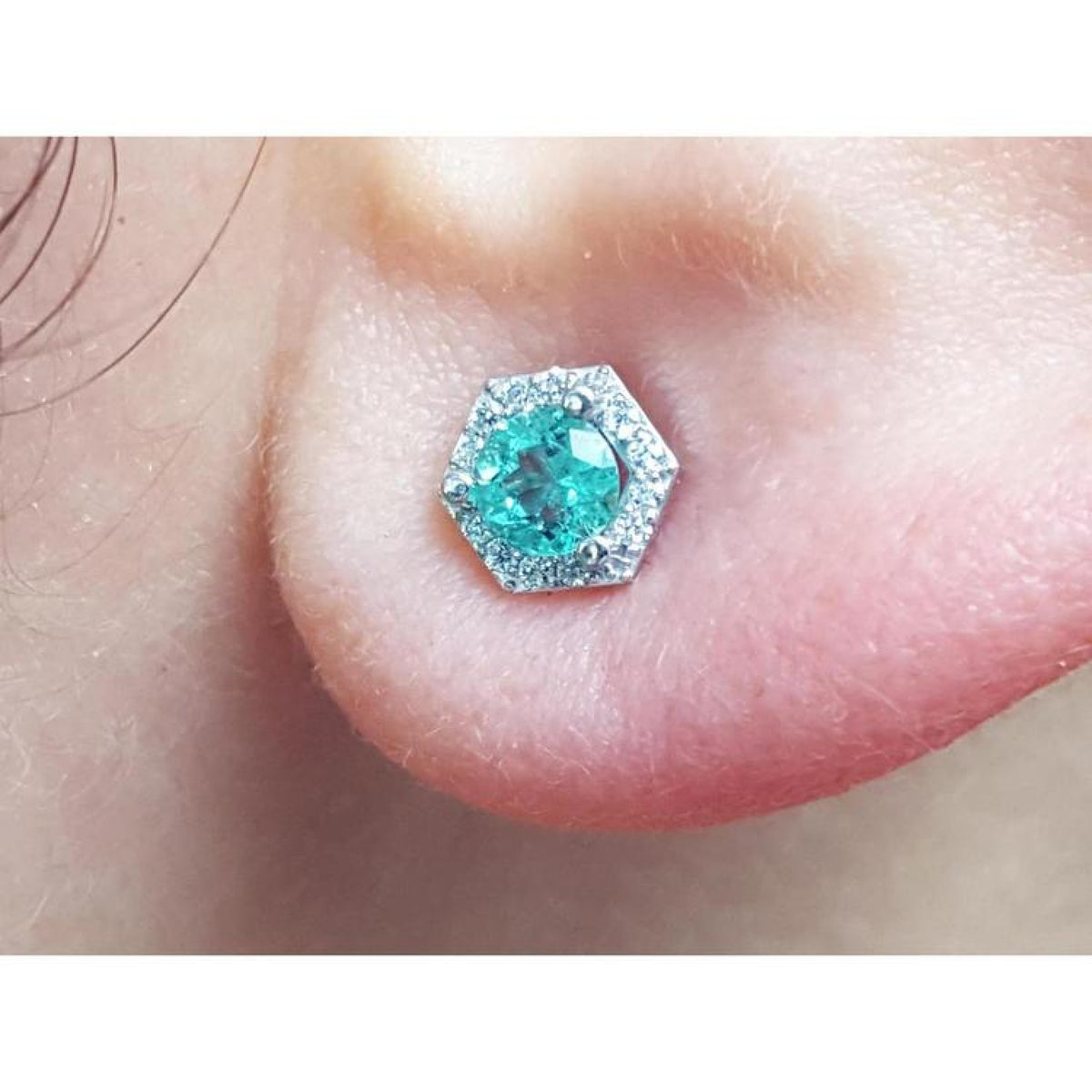 An earlobe dressing a natural emerald stud earring with a geometric halo diamond.