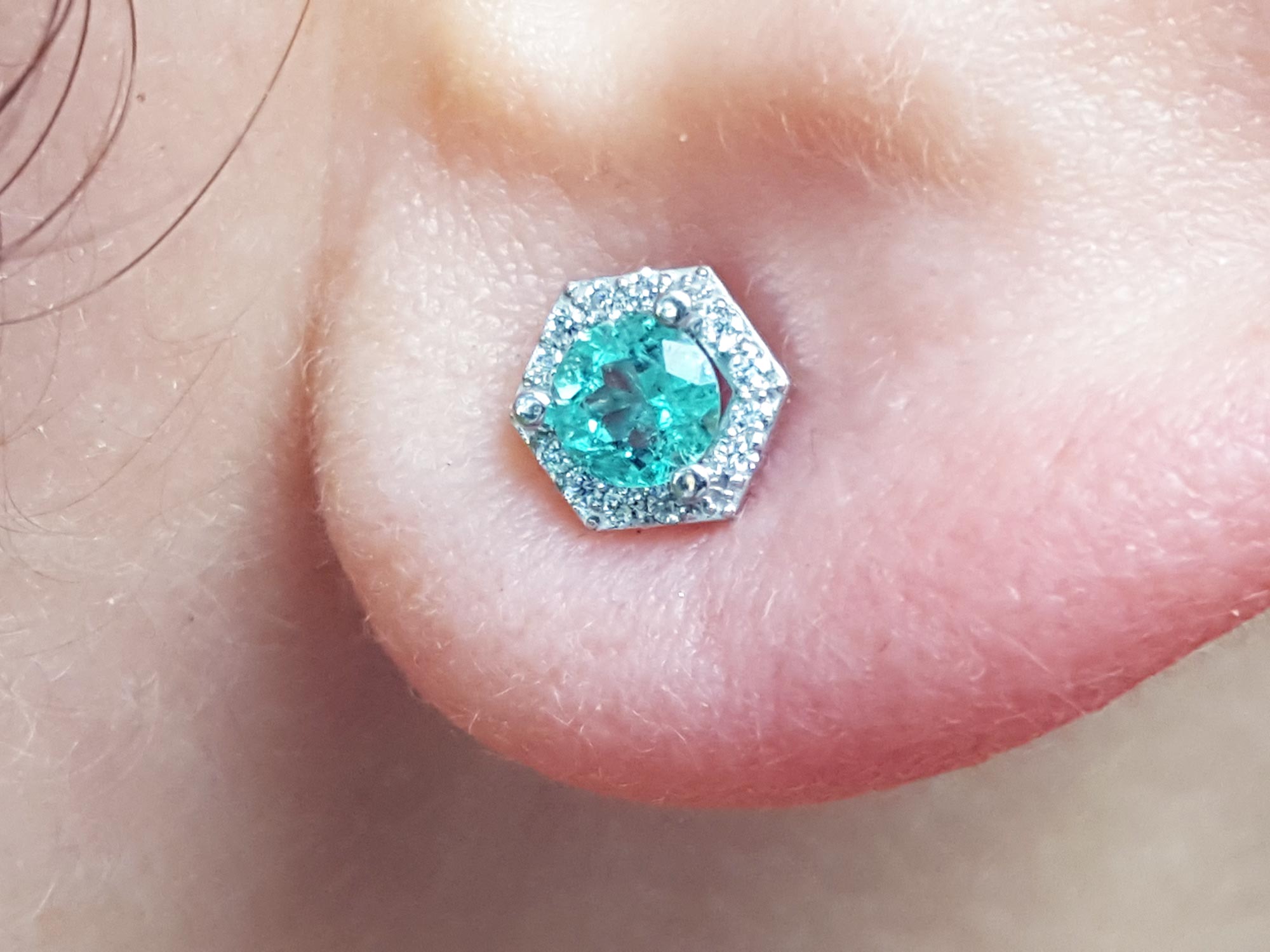An earlobe dressing a natural emerald stud earring with a geometric halo diamond.