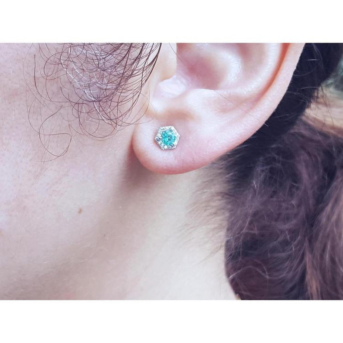 14K white gold stud earring with a round teal gemstone surrounded by tiny white stones, worn on an ear.