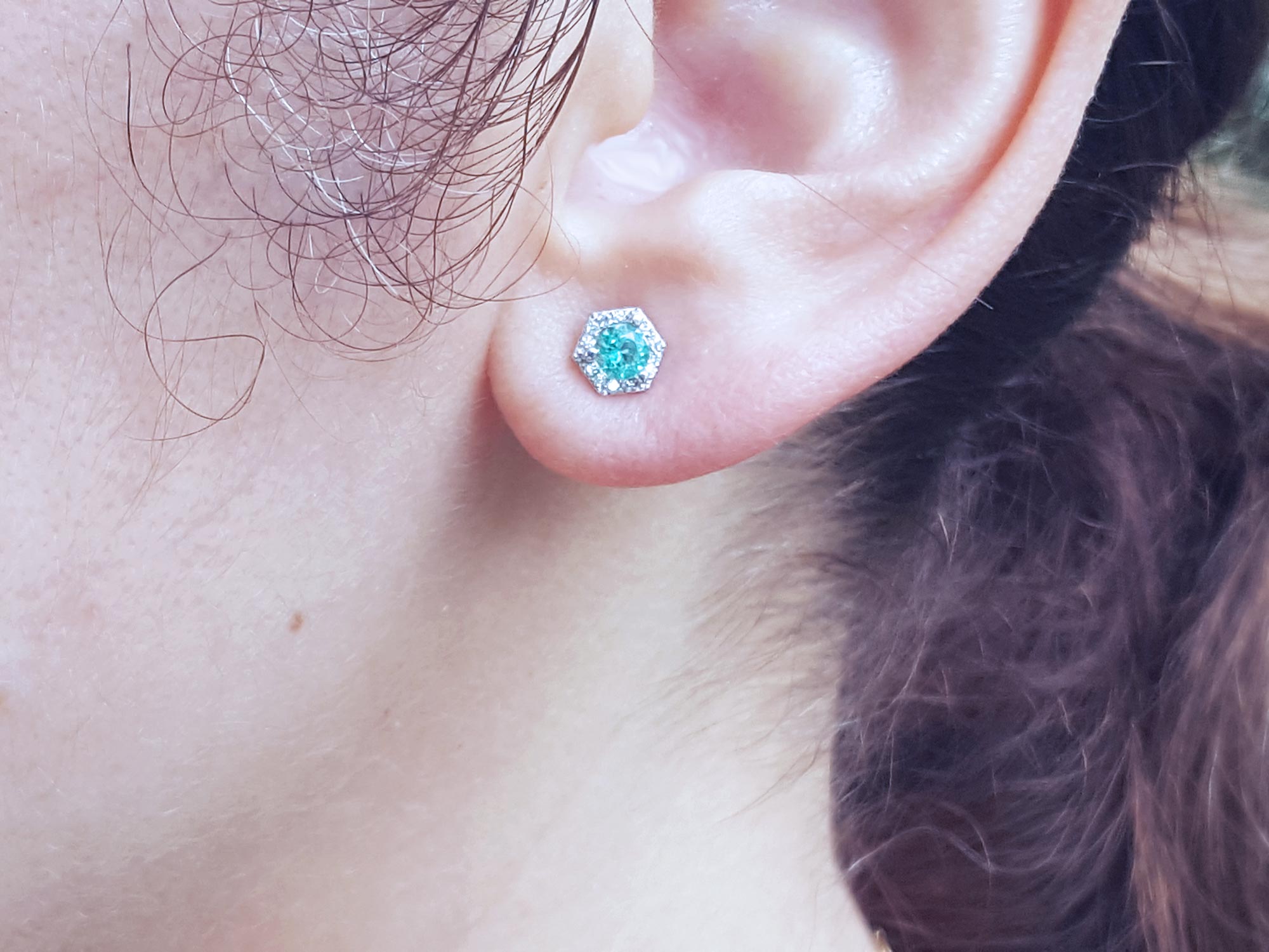 A woman&#39;s ear dressing a stud emerald earring with hexagonal halo diamond.