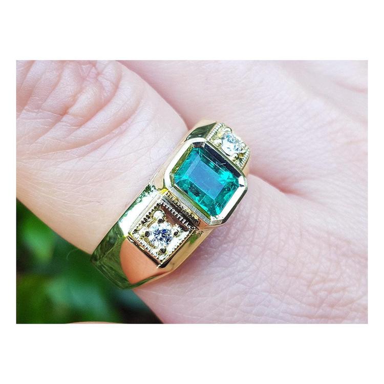 An 18k yellow gold men’s ring featuring a genuine Colombian emerald and side diamonds, elegantly worn on a finger.