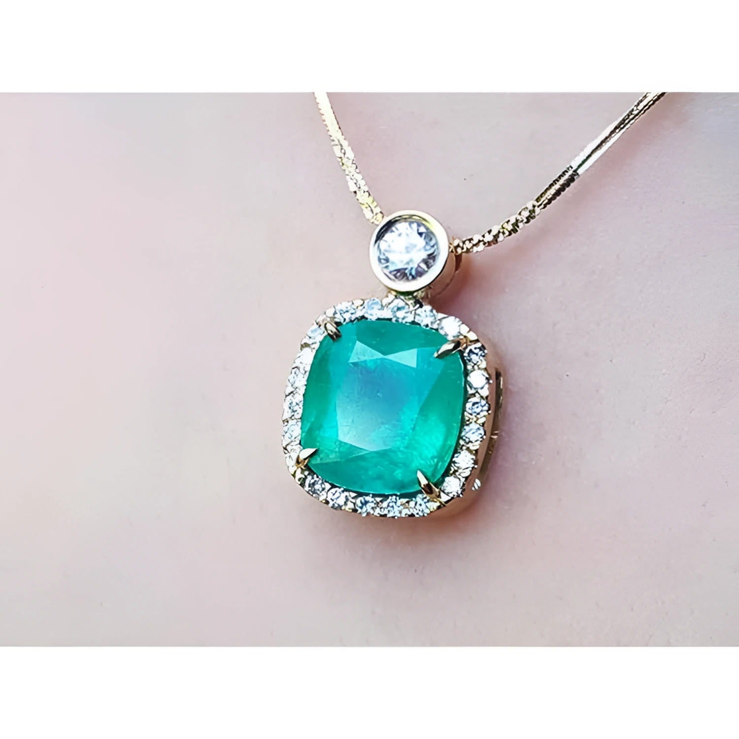 Cushion cut emerald necklace in 18K yellow gold with halo diamonds and a single diamond accent.