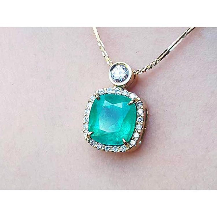 Cushion cut emerald necklace in 18K yellow gold with halo diamonds and a single diamond accent.