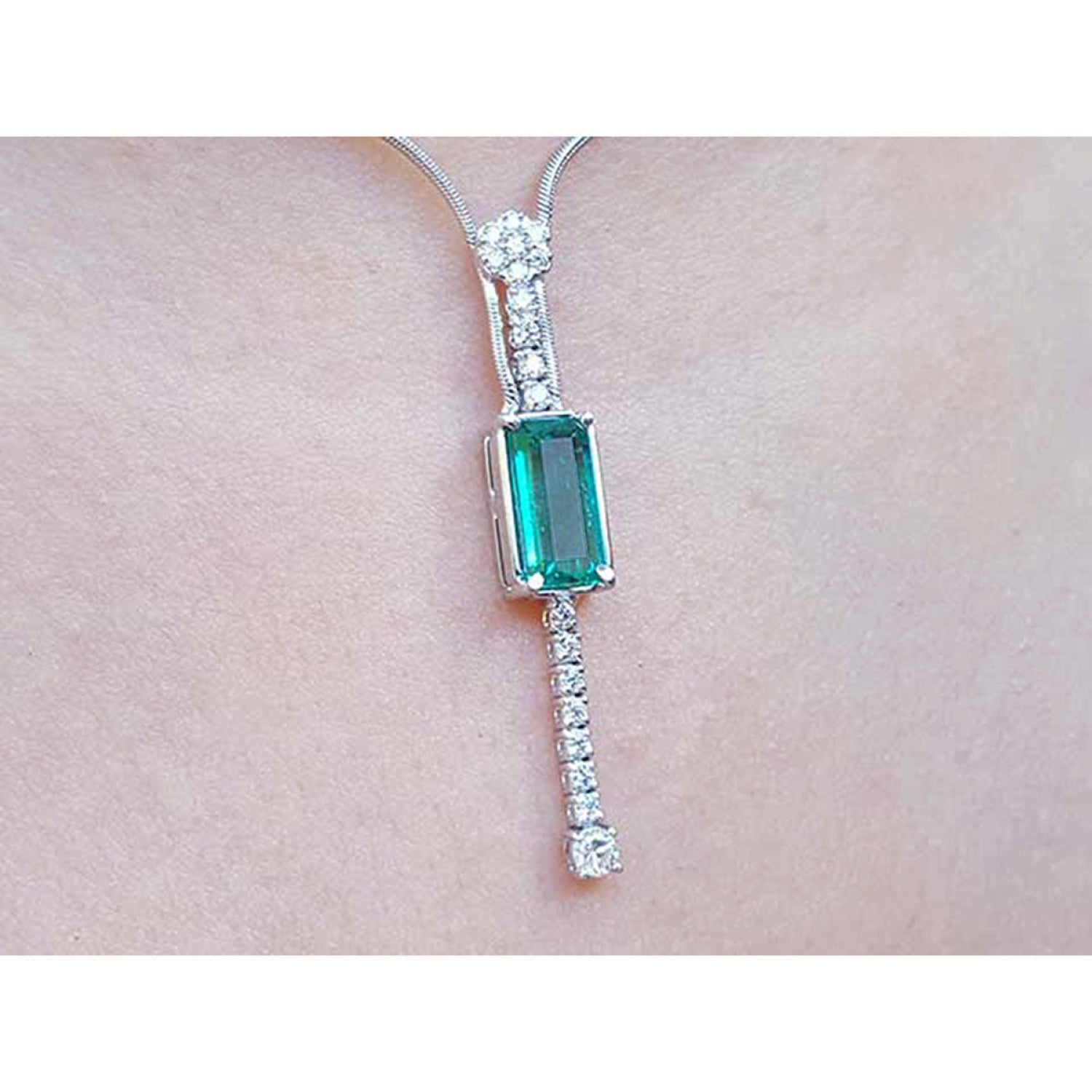 White gold women's necklace with a rectangular Colombian emerald and diamond accents, worn on a neck.