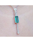 White gold women's necklace with a rectangular Colombian emerald and diamond accents, worn on a neck.