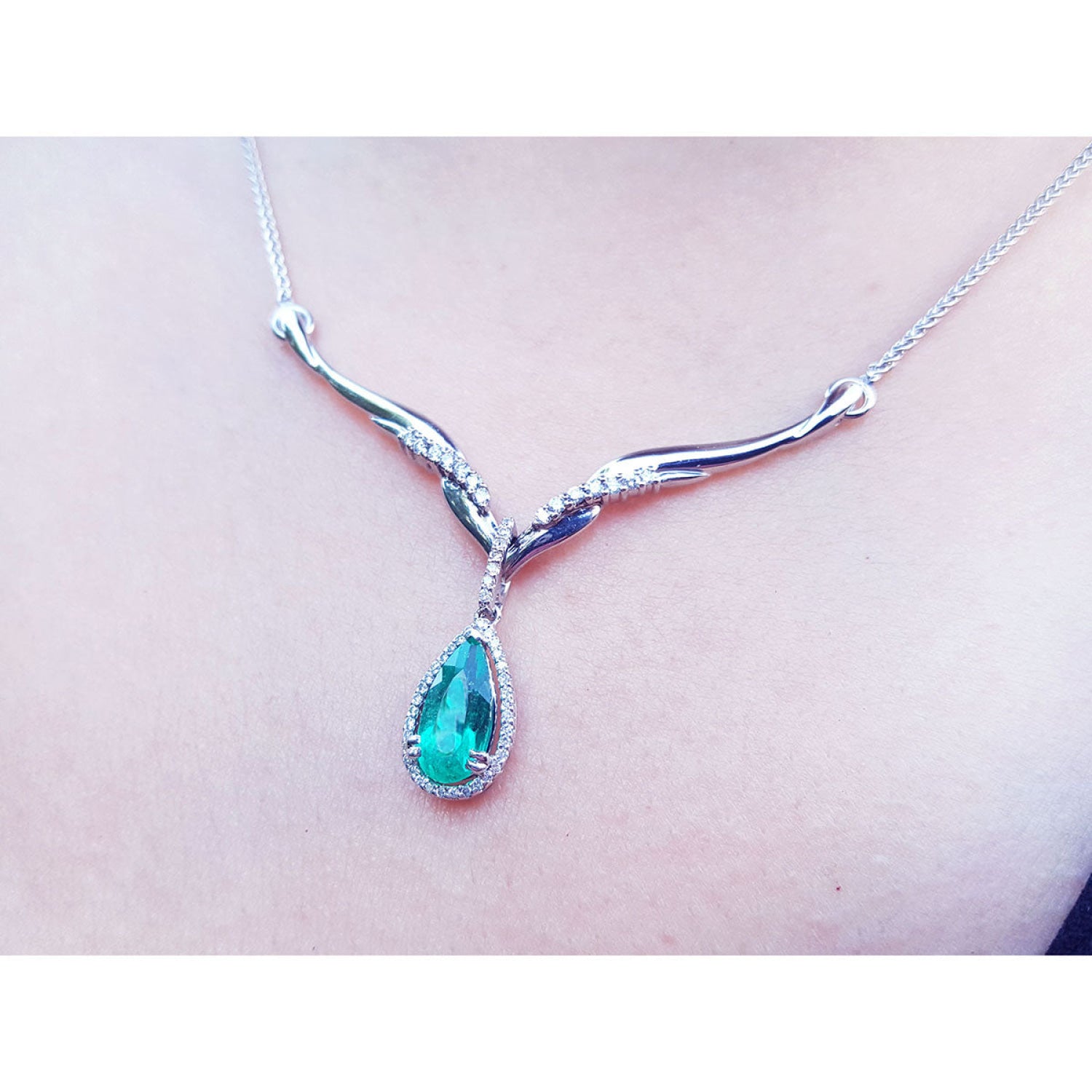 14K white gold necklace with a pear-cut emerald pendant surrounded by diamonds and an entwined chevron design.