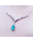 14K white gold necklace with a pear-cut emerald pendant surrounded by diamonds and an entwined chevron design.