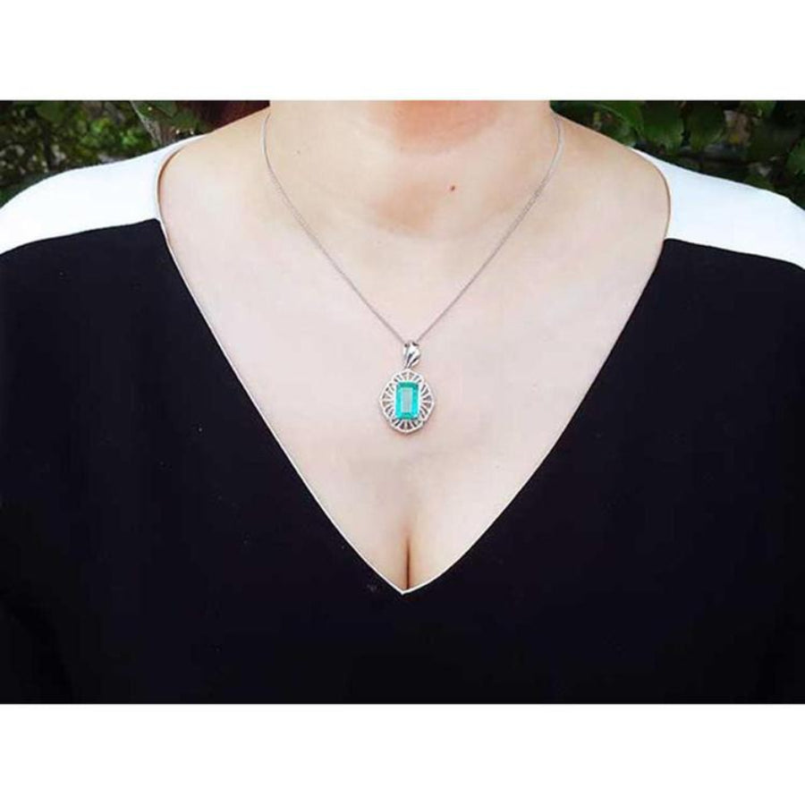 Emerald-cut Colombian emerald pendant with natural diamonds in 14K white gold on a woman's neck.