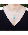 Emerald-cut Colombian emerald pendant with natural diamonds in 14K white gold on a woman's neck.