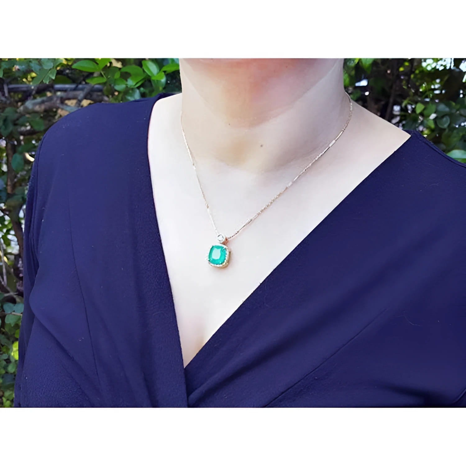 Cushion cut emerald necklace with halo diamonds in 18K yellow gold on a person.
