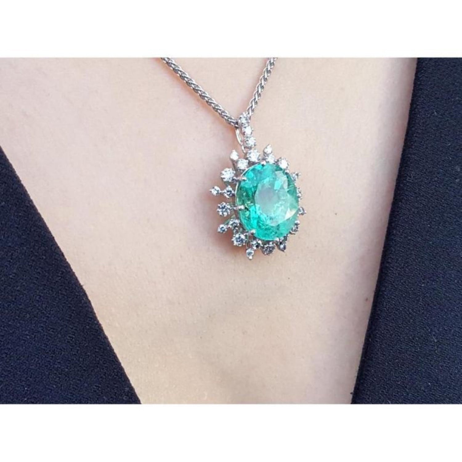 Oval cut medium light green emerald pendant with halo diamonds in 14K white gold on a necklace.