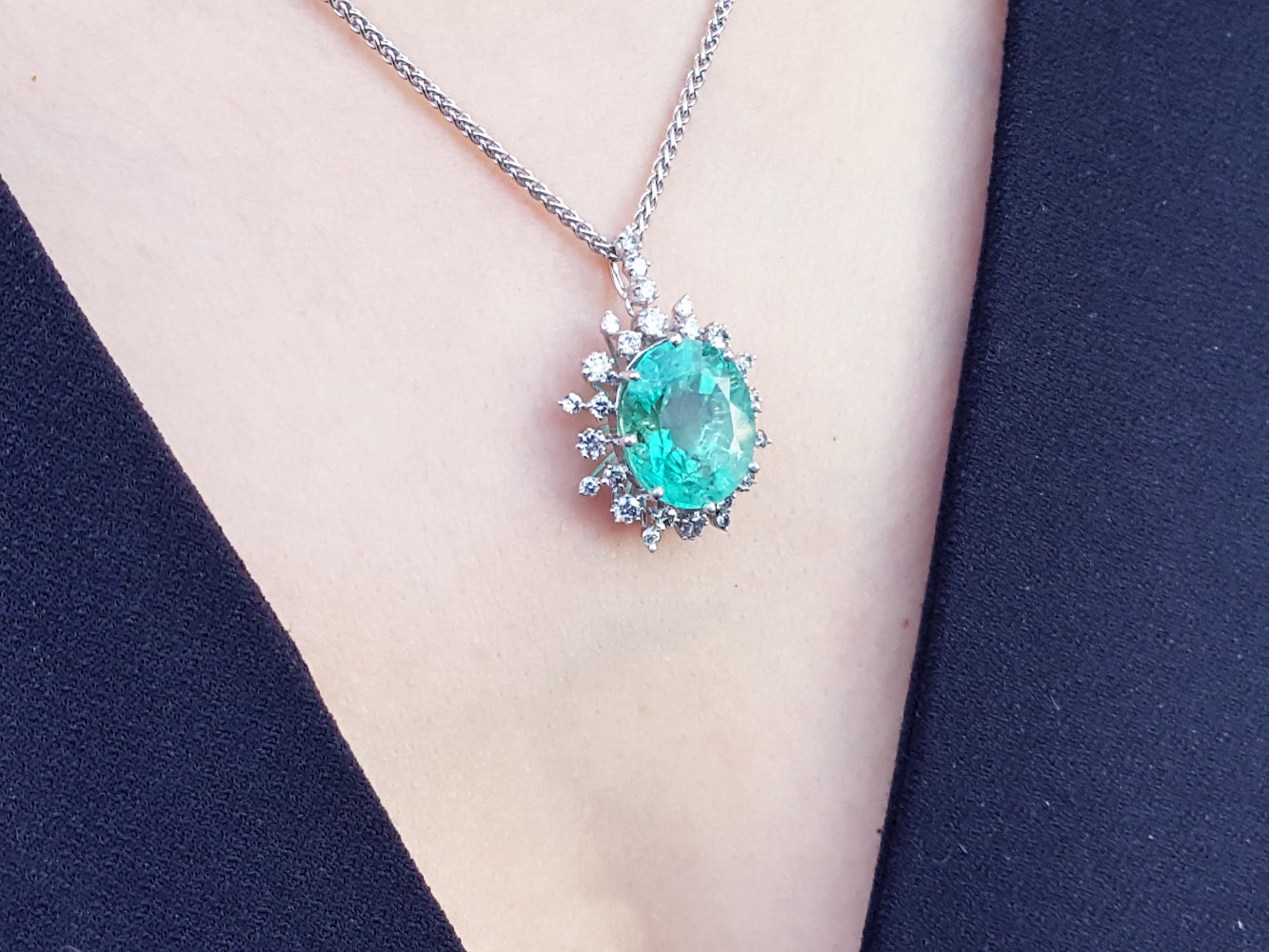 Necklace with a natural oval emerald pendant on a person&#39;s neck against a black background