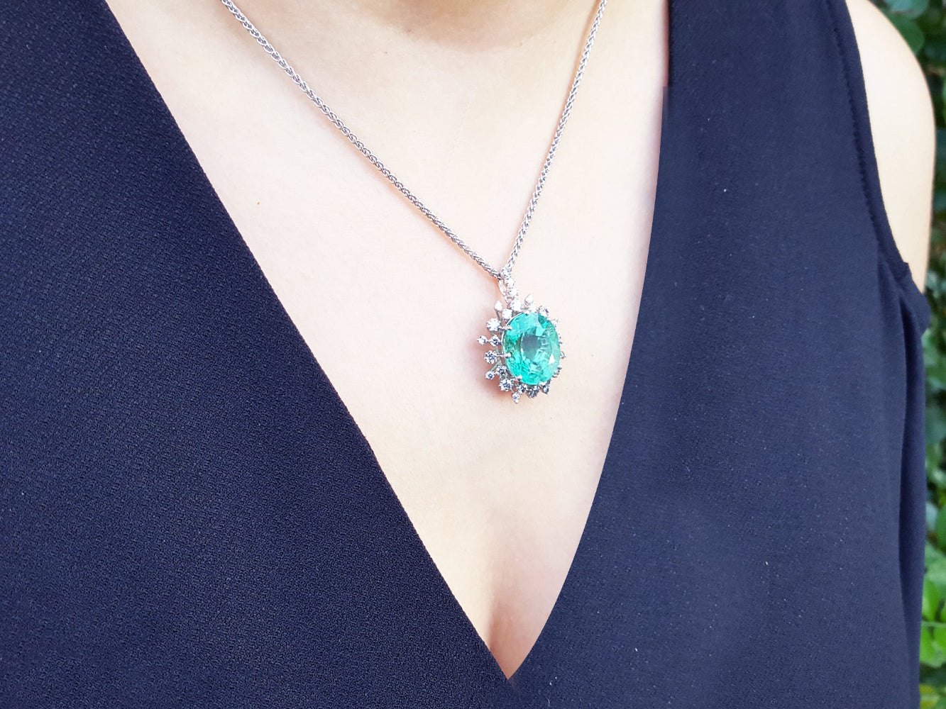 An oval emerald pendant necklace on a person wearing a dark blue dress.