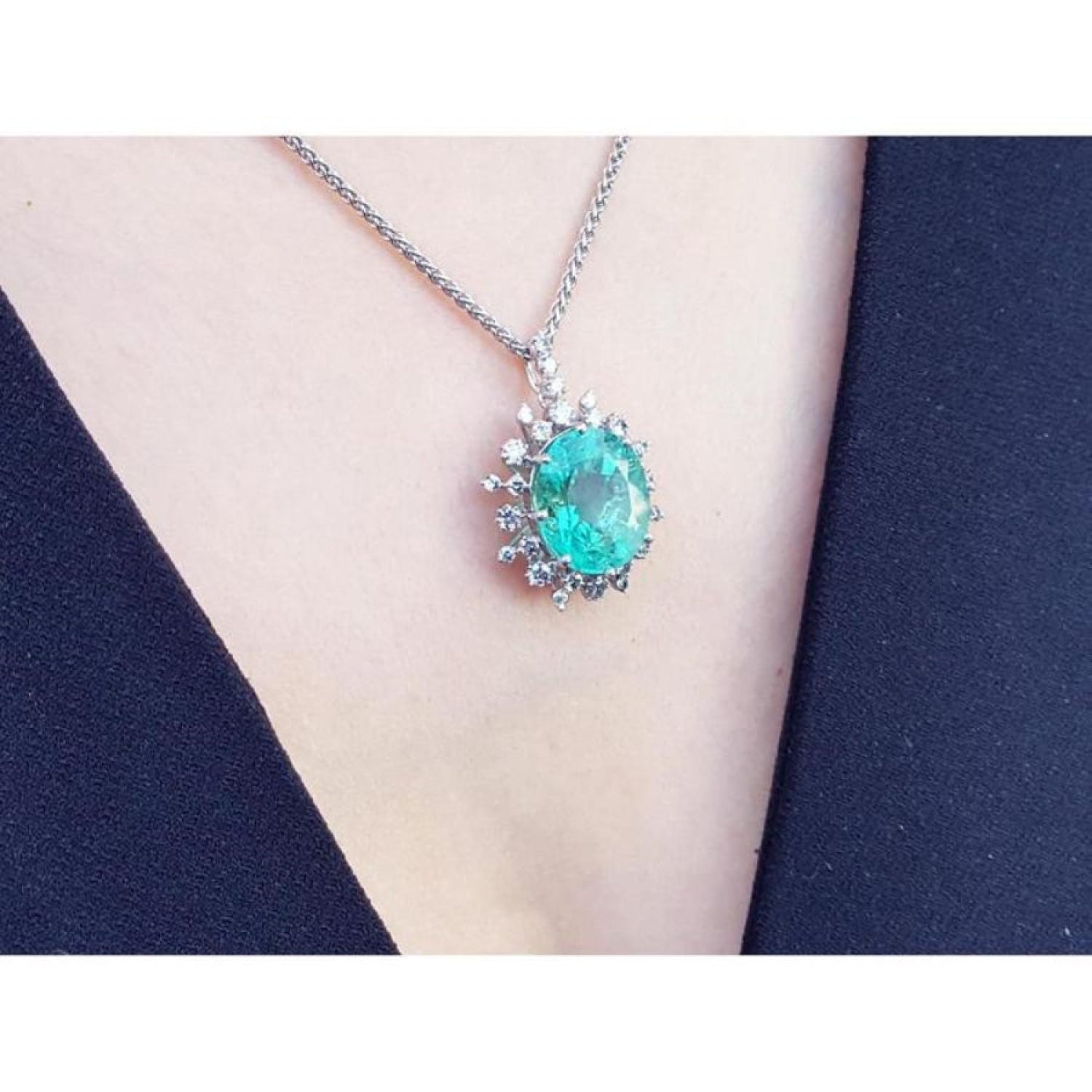 Oval cut medium light green emerald pendant with halo diamonds in 14K white gold on a chain.