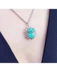 Oval cut medium light green emerald pendant with halo diamonds in 14K white gold on a chain.
