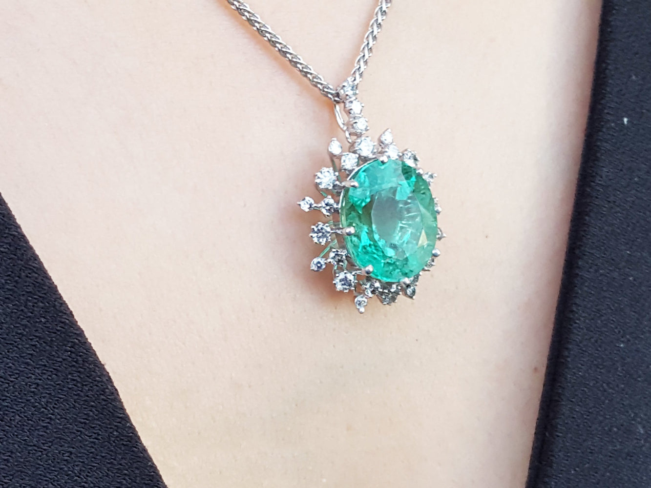 Emerald pendant necklace on a person's neck with a plain background