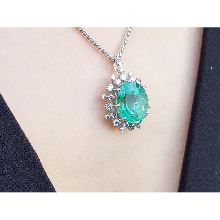 Emerald pendant necklace on a person's neck with a plain background